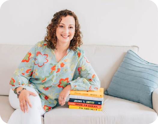 Woman sitting posed on a couch with one hand resting on a stack of books.