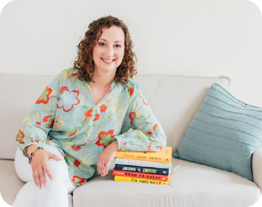 Woman sitting posed on a couch with one hand resting on a stack of books.